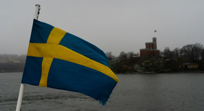 a flag of sweden and a building of some sort is seen near the water