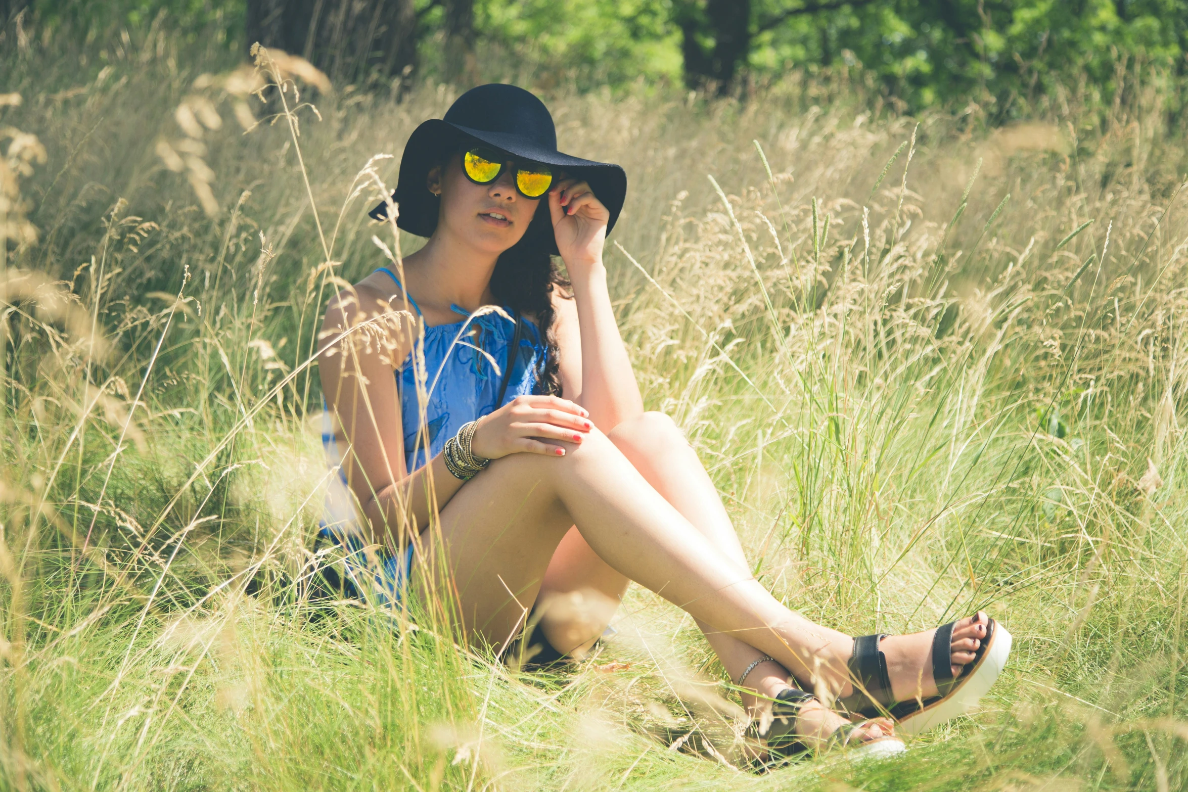 a young woman sits in the tall grass with her hat on