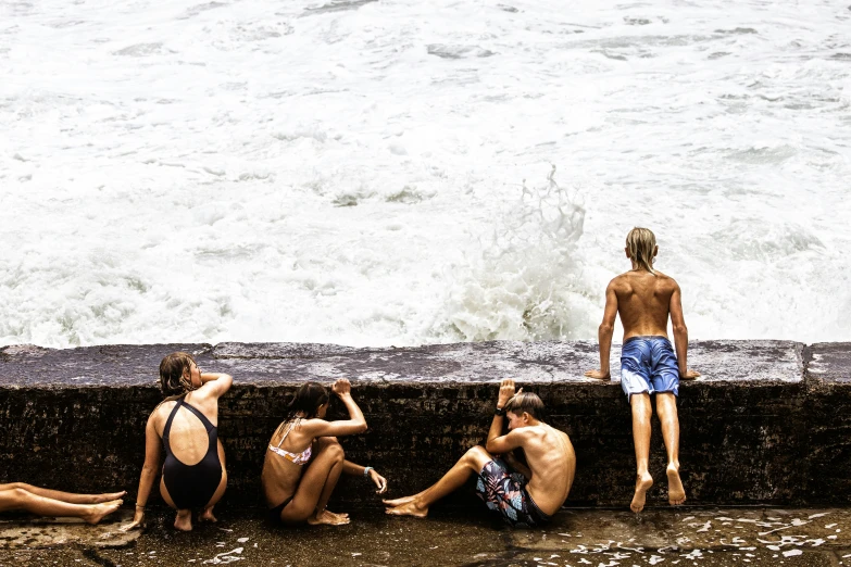 several men sitting next to the ocean watching waves crash