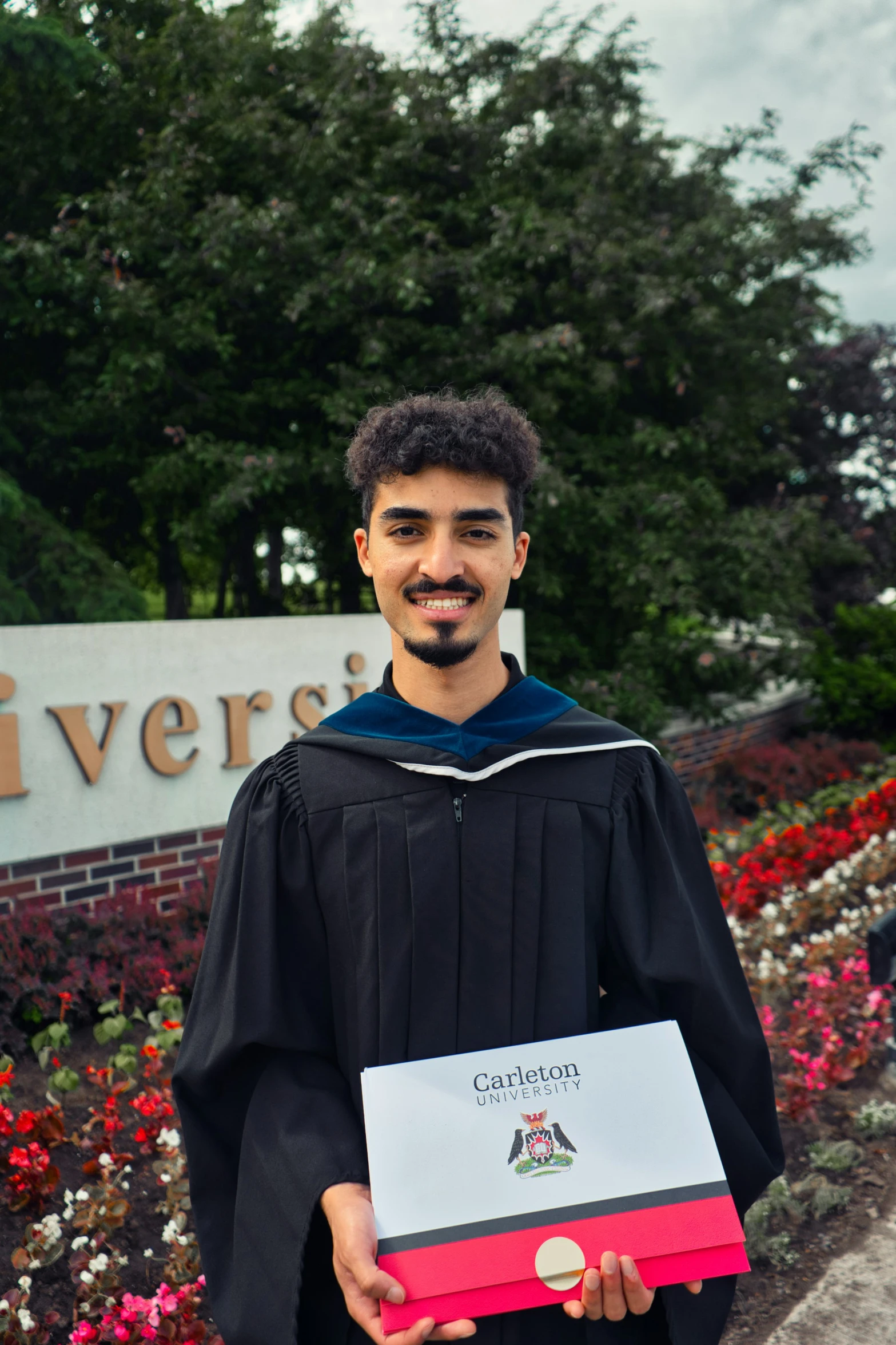 a male in a black and white gown holds up his graduation paper