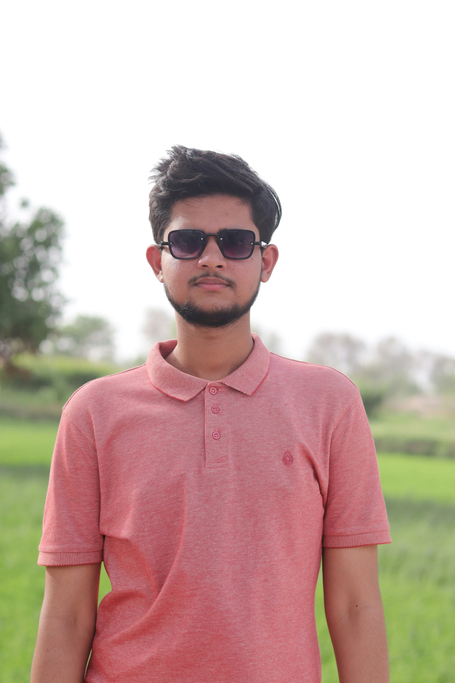 a man wearing sunglasses standing next to a lush green field