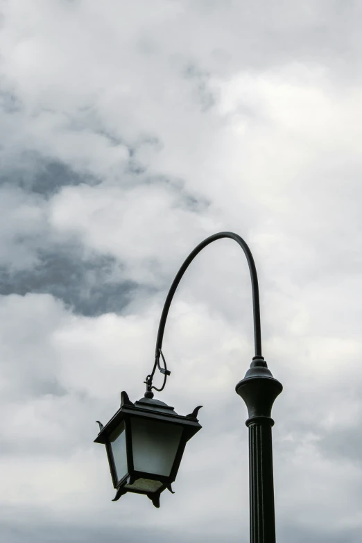 the street light is lit against the cloudy sky