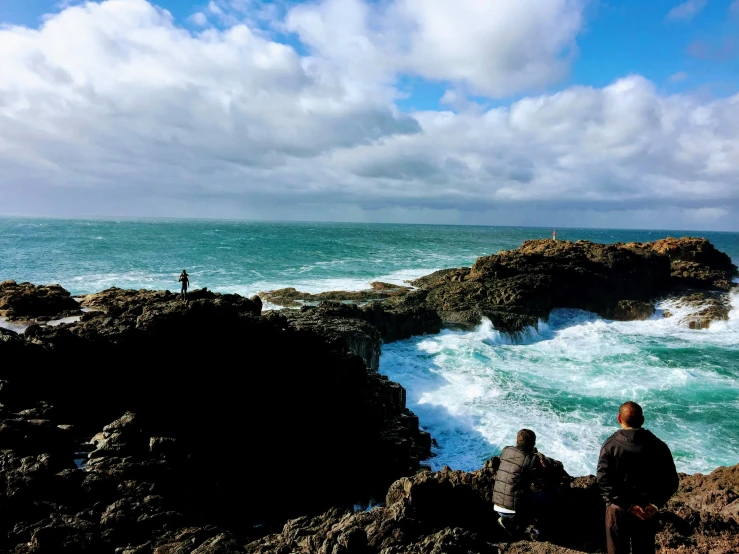 two people sitting by the water and some rocks