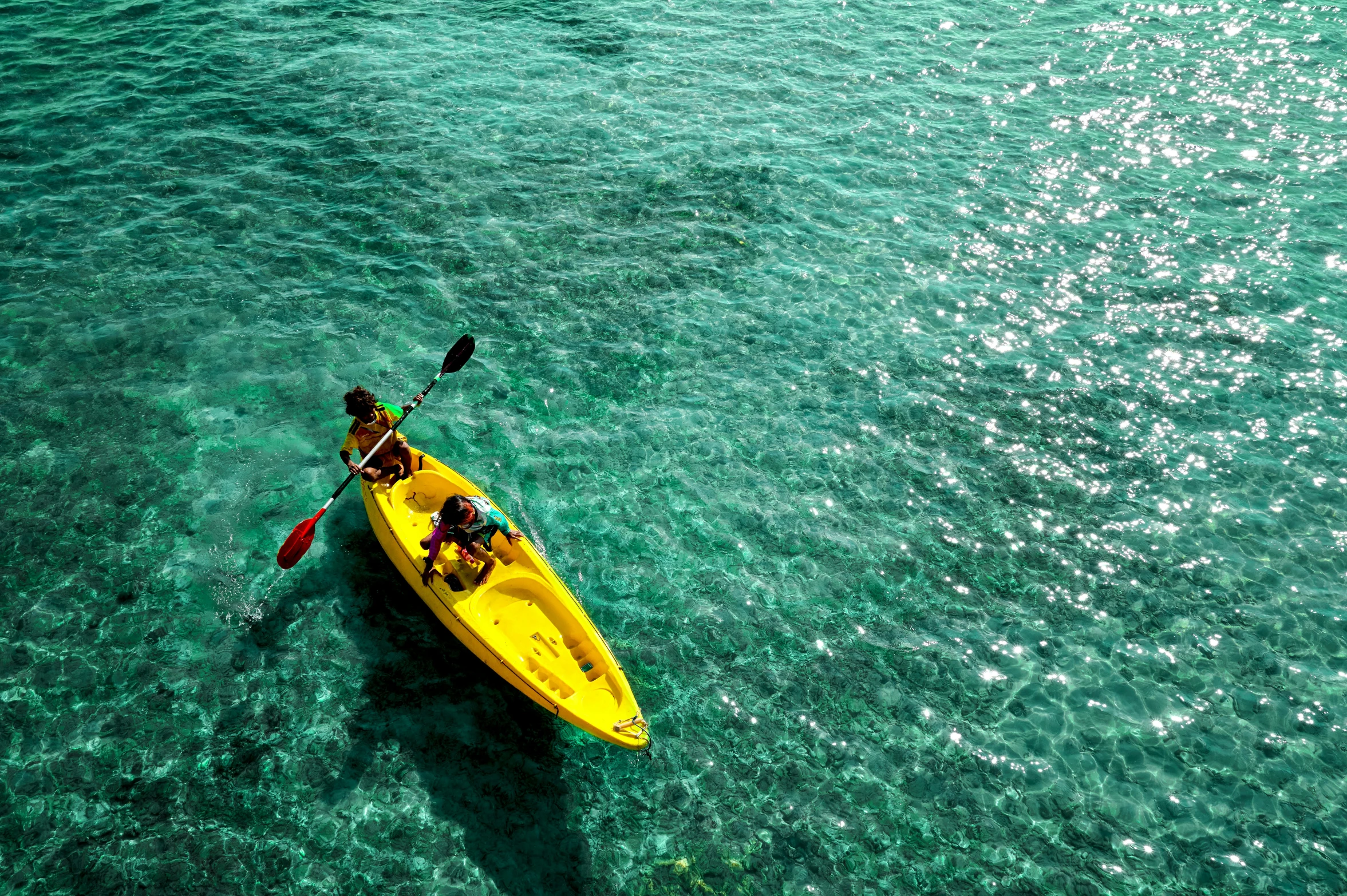 two people are paddling down on a yellow kayak