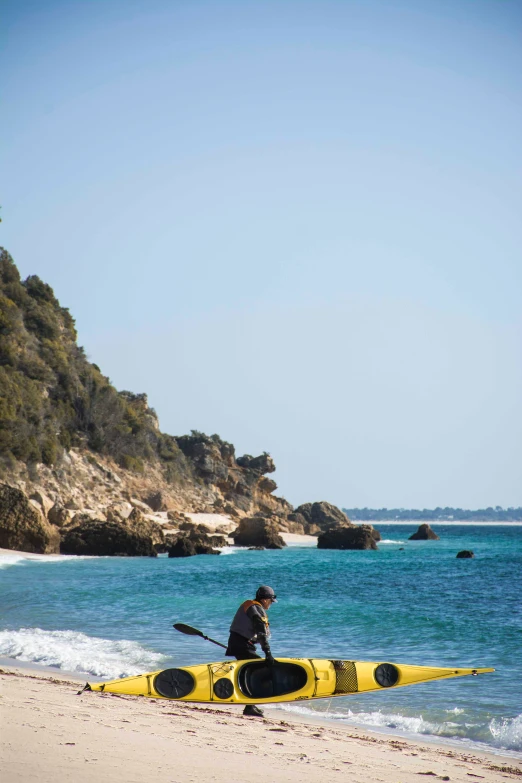 a man riding a kayak on the beach next to a cliff