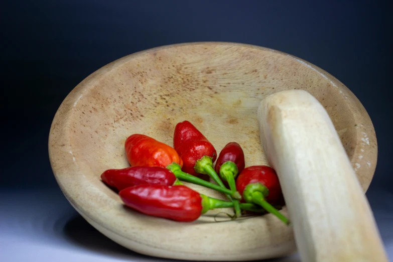 peppers are in a bowl with one wooden spoon