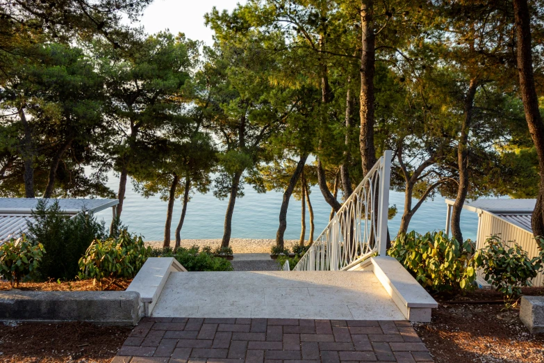 a white fenced in walkway leading to trees next to the water