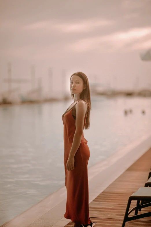 a woman in an orange dress is on a pier by the water