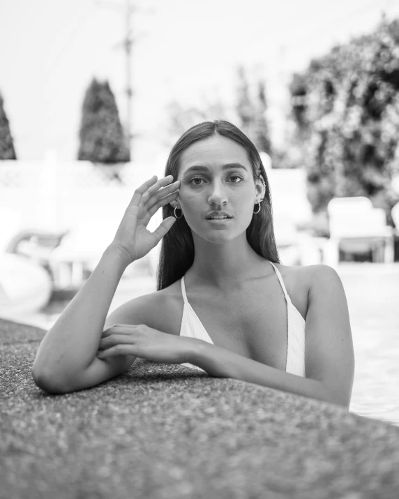 the girl is posing next to the pool with her hand in her hair