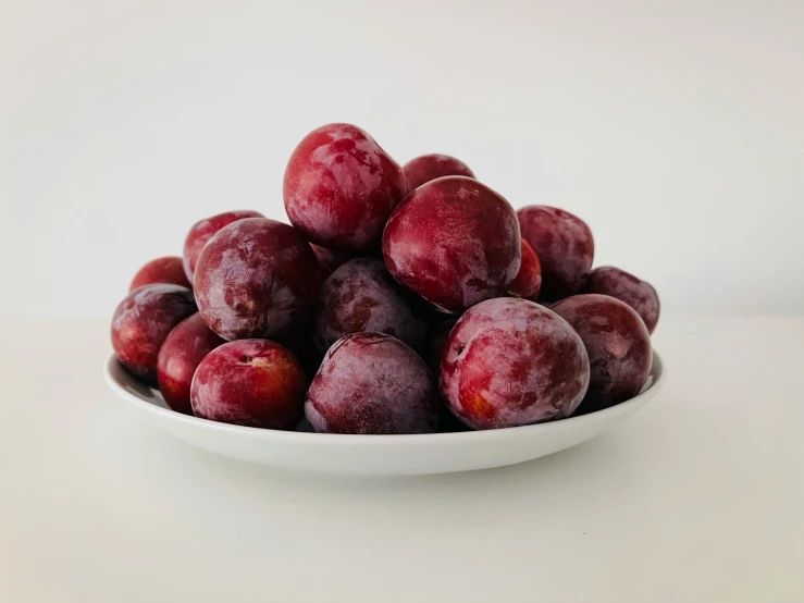 a bowl filled with plums is shown on a table