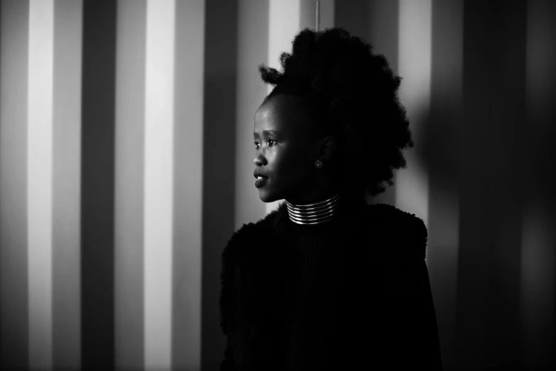 a woman wearing a necklace stands by a wall