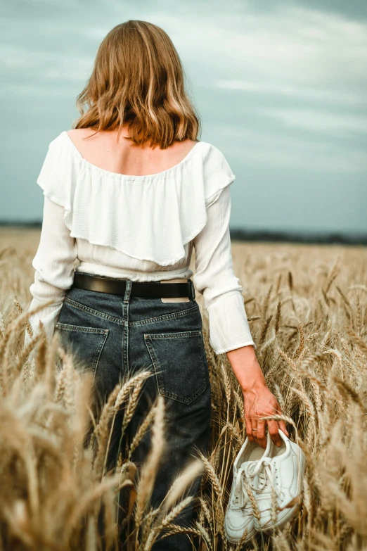 a woman walking through an empty wheat field holding a white purse