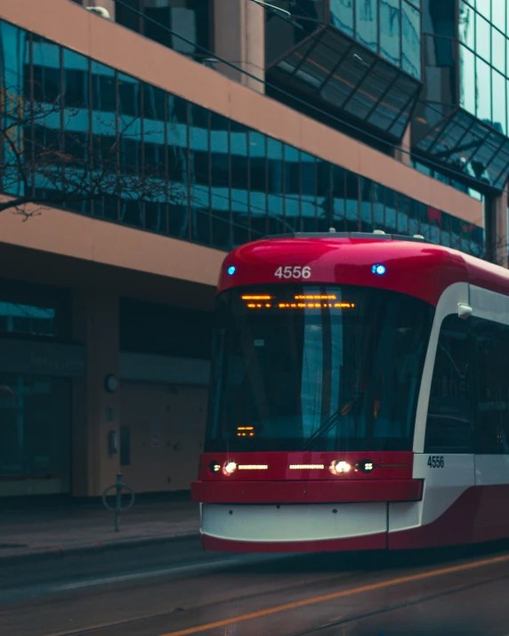 a red city bus on the tracks next to tall buildings