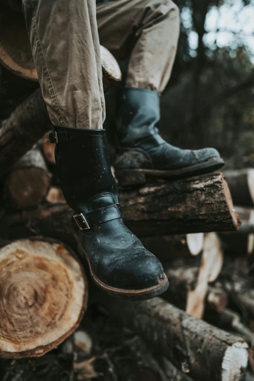 a person wearing black boots on top of wooden logs