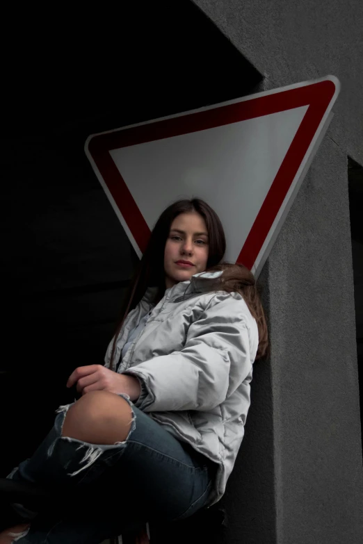 girl sitting under a street sign and leaning against it