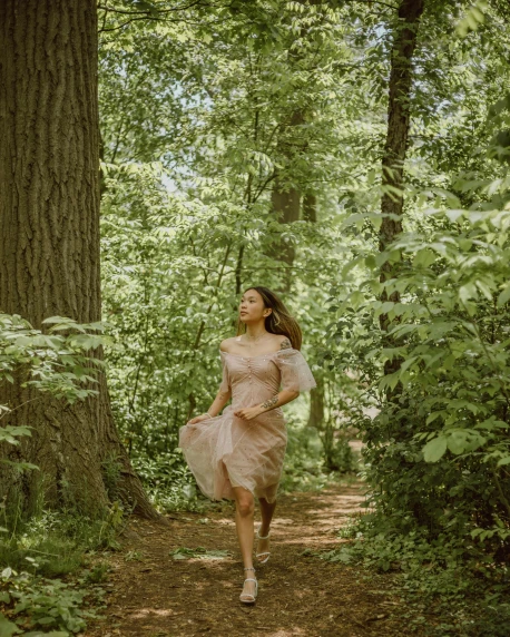 a woman is walking through the woods with a pink dress