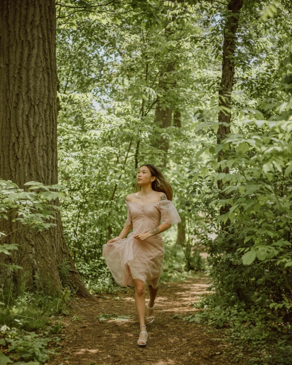 a woman is walking through the woods with a pink dress