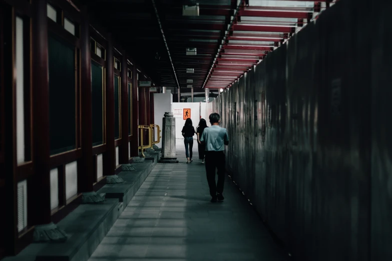 three people walking down a walkway in a train station