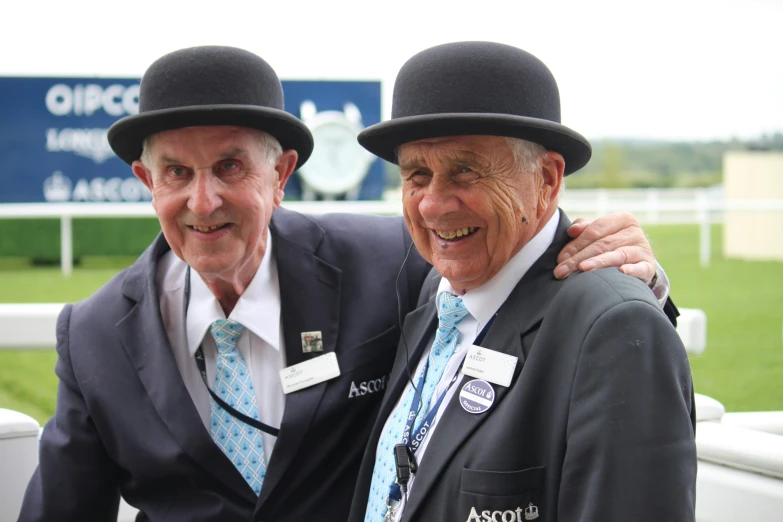 two older men in suits and hats smile at the camera