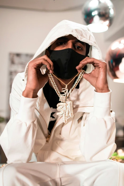 a man in white clothing is wearing jewelry and covering his face with his jacket