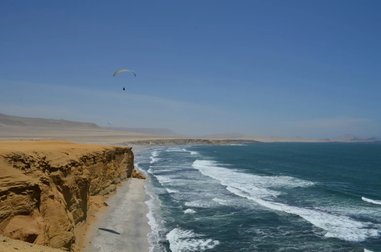 a parasailer flying over an ocean cliff near the shore