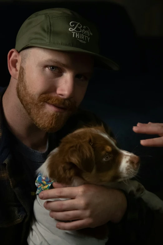 a man with a beard holds a puppy and looks off into the distance