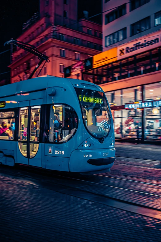 a blue tram at night with buildings in the background