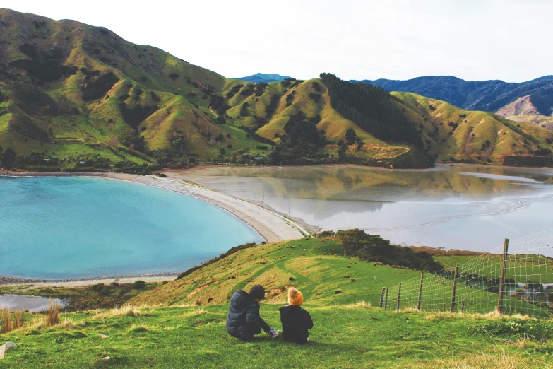 the people are standing on the green hill above the lake