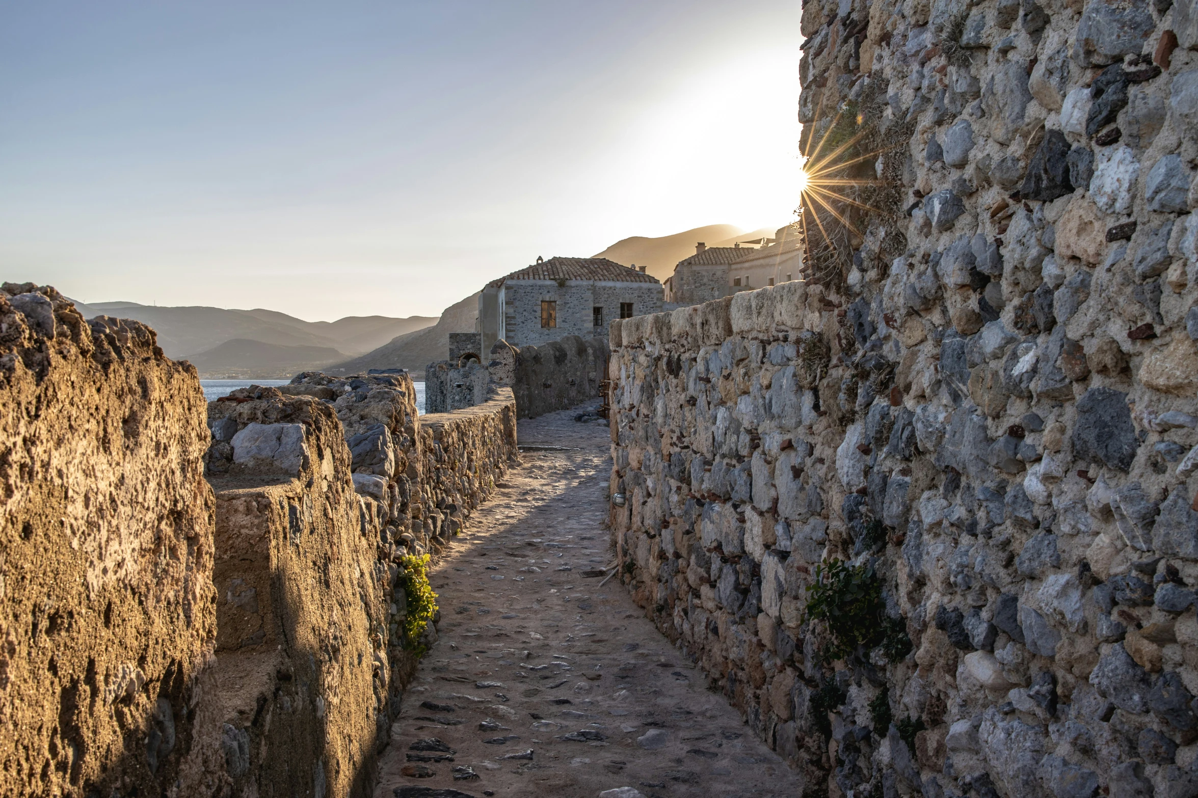 a narrow cobblestone road with sun rising above the horizon