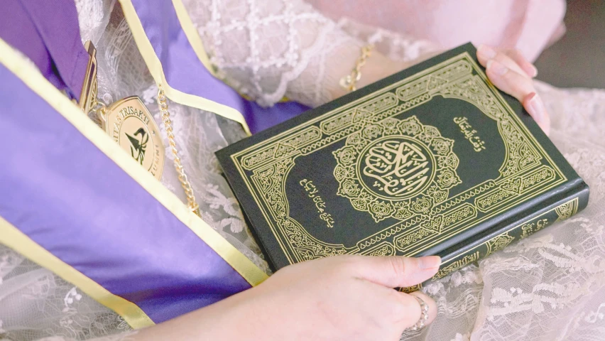 a woman is holding a book with arabic writing on it