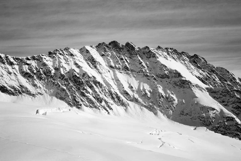 a long mountain covered in snow next to a cloud filled sky