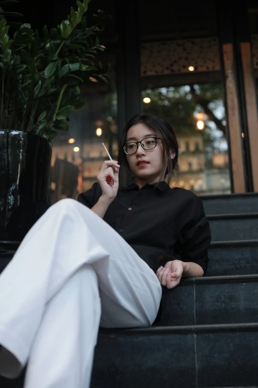 a woman sitting on a step smoking and leaning against her glass door