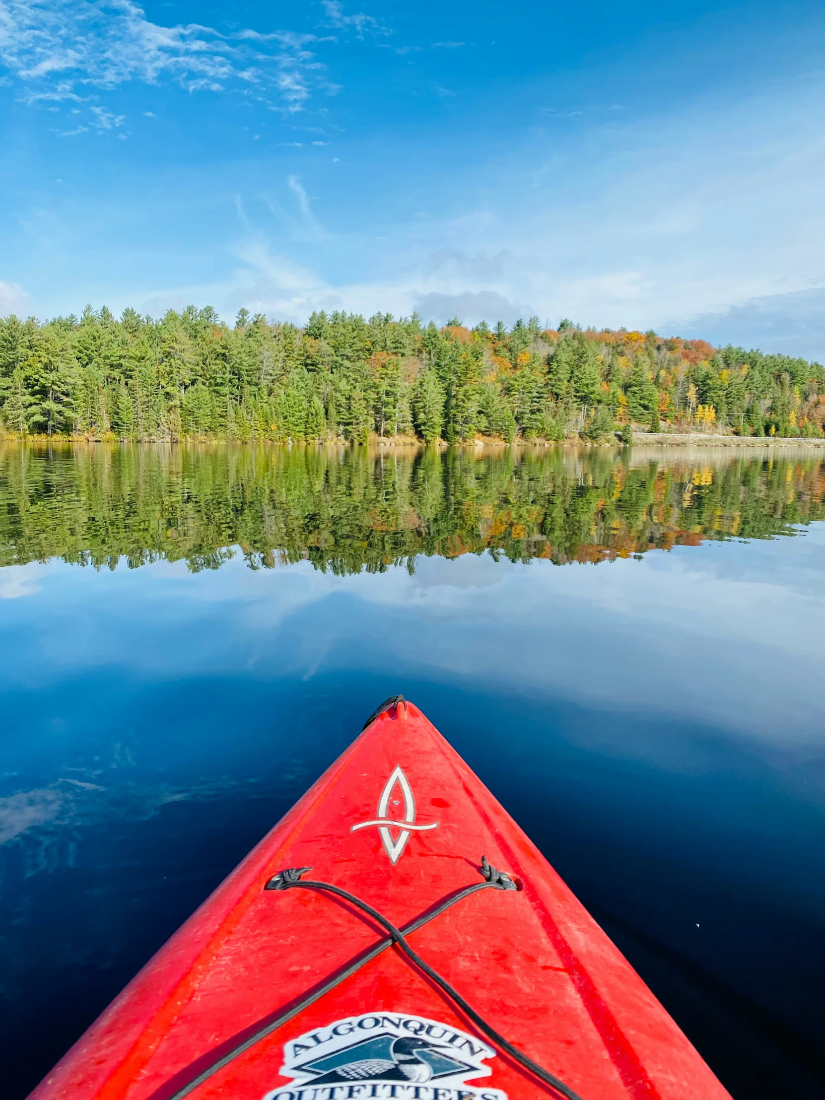 a red kayak sitting in front of a forest filled lake