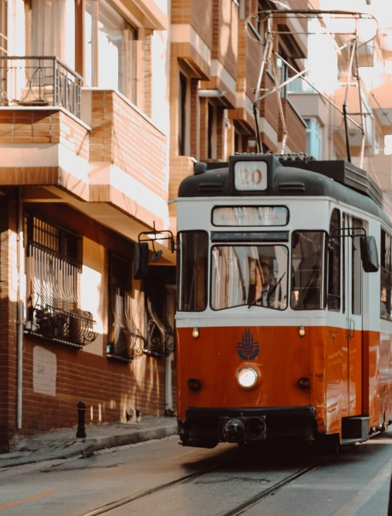 an orange and white tram riding on the tracks in a street