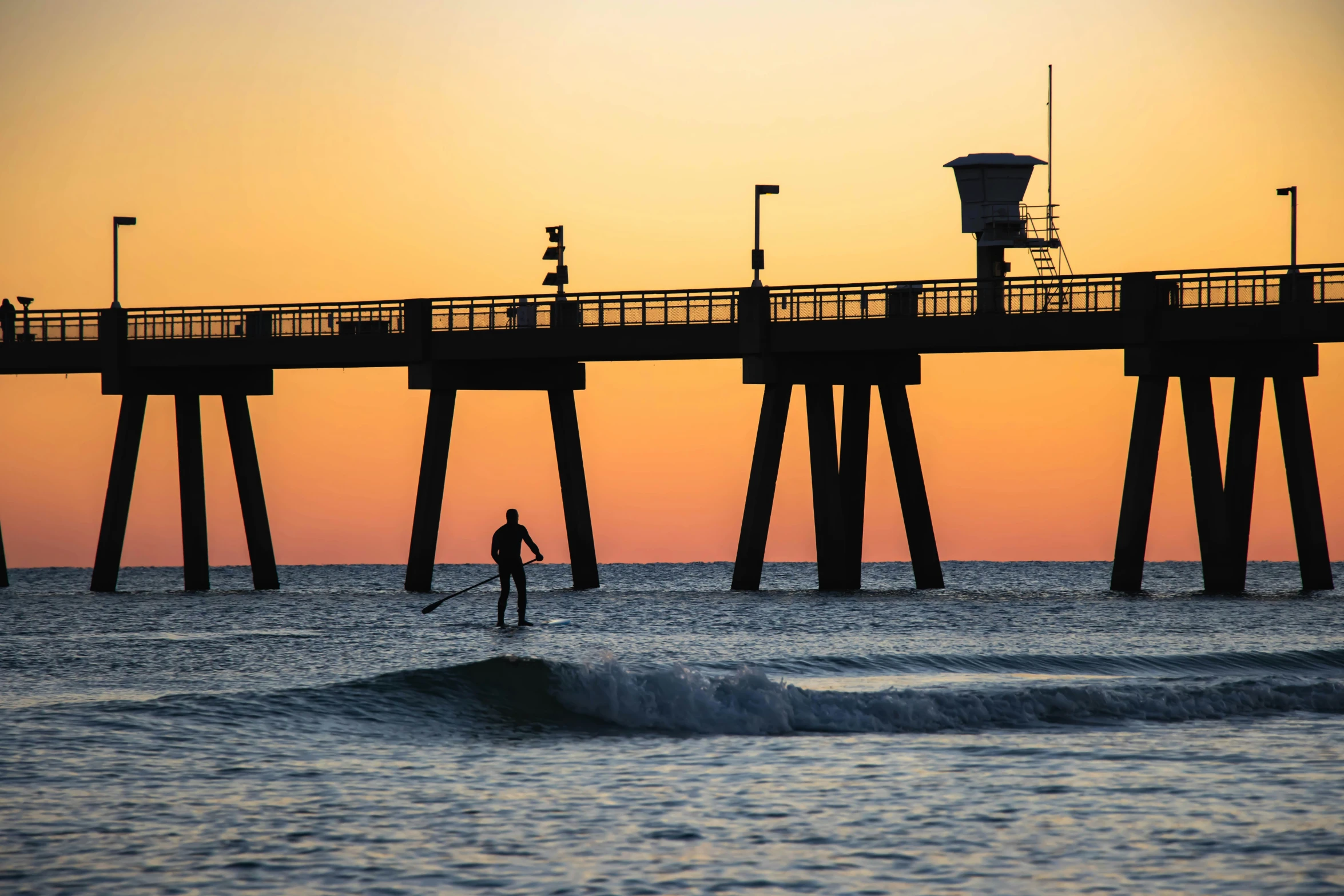 a person surfboarding in the ocean next to a pier