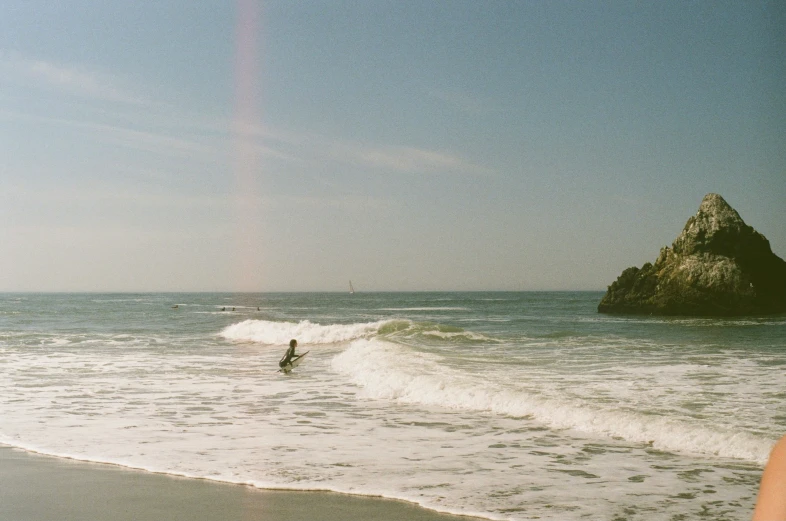 a surfer in the surf near some rocks on a sunny day