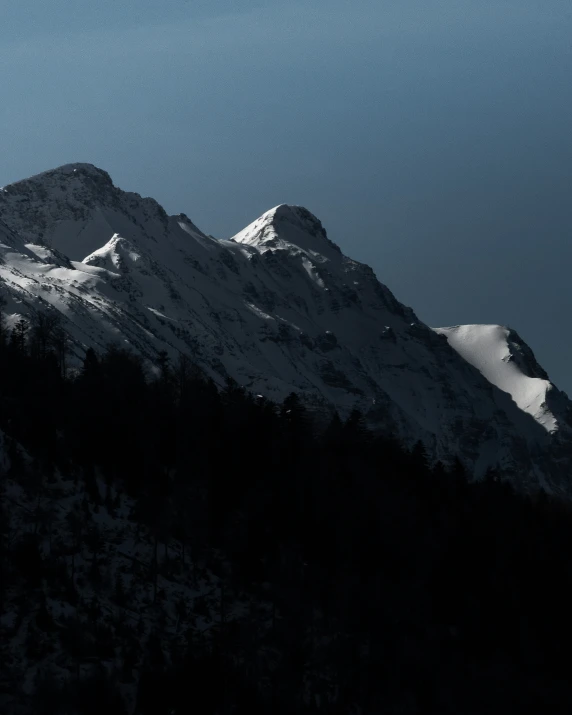 the mountaintop of a snow capped mountain is silhouetted against the dark blue sky