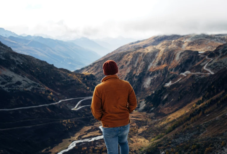 man looking down over a mountain pass with a view of mountains in the distance