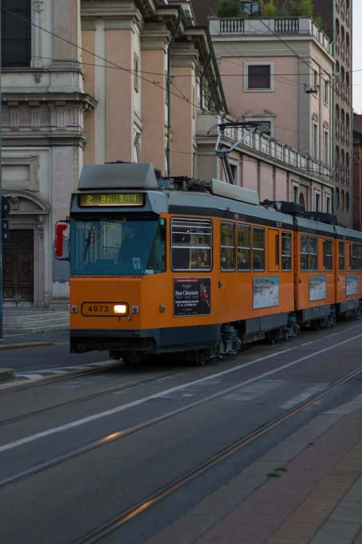 an orange and black train traveling past buildings