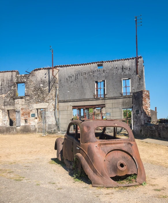 an old rusted down car is parked in a lot with buildings and wires