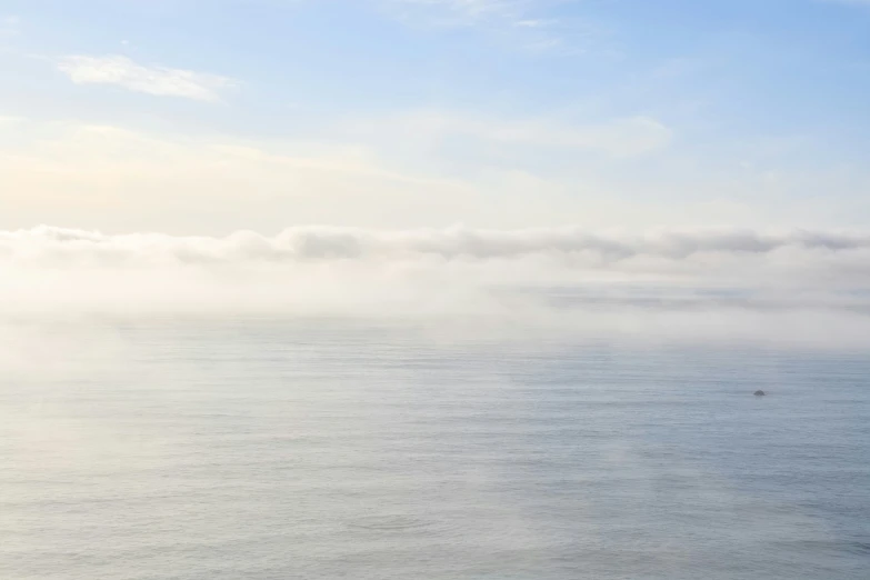 an ocean with some fog in the sky and a ship on the water