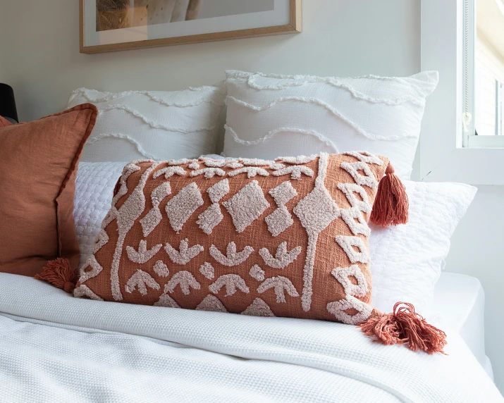 a bed with a white blanket and orange throw pillows
