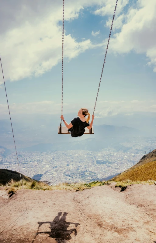 a woman swings on a swing set with a view of the city below