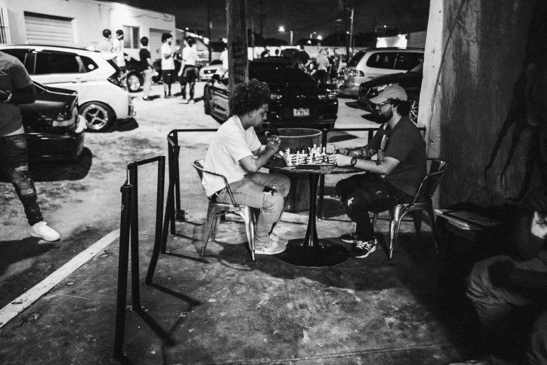 two men sitting at a table playing chess in the street