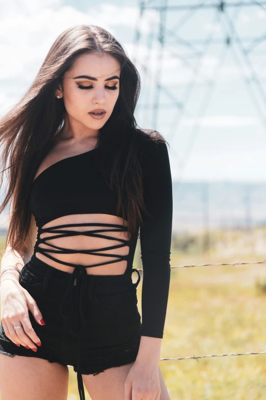 a woman standing next to a wire fence wearing a black top and shorts