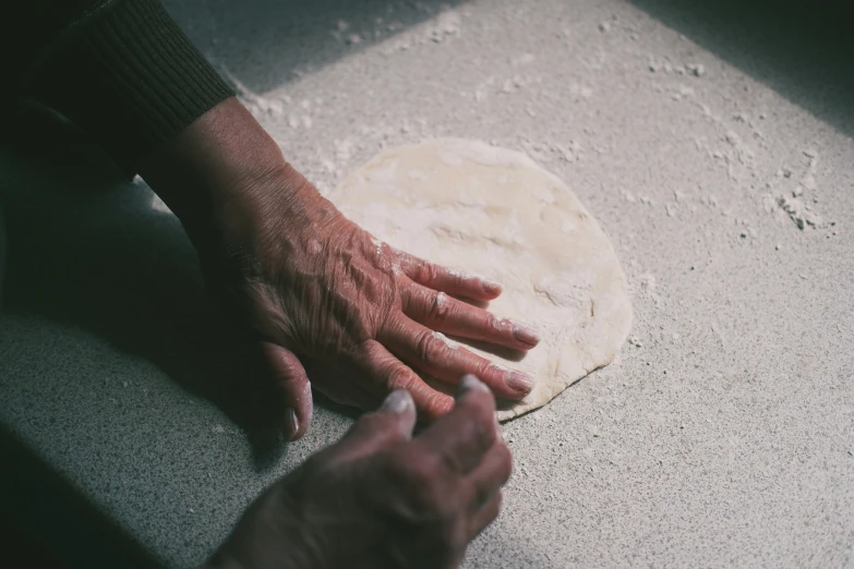 an elderly person rubbing their hands on top of a dough