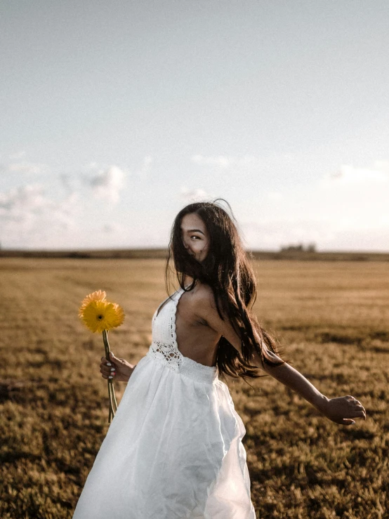 woman in a white dress holding yellow flowers on the field