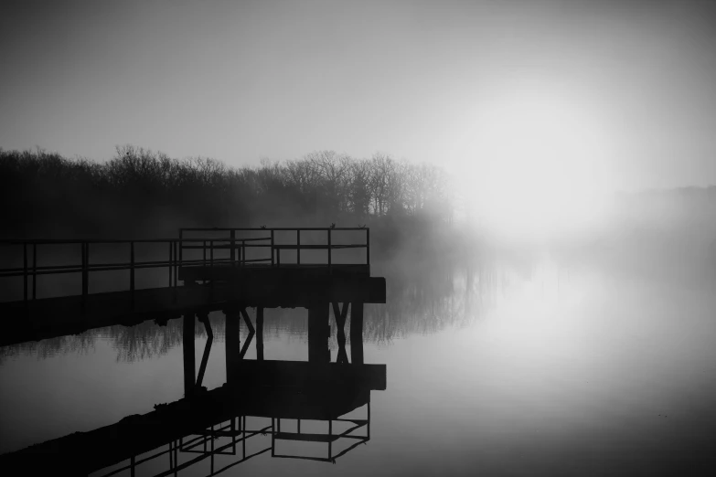 a lake in fog, with the sun shining over the water and bridge