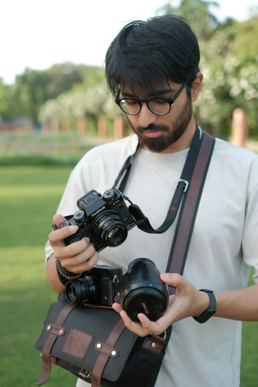 a man in glasses and a white shirt is holding two cameras