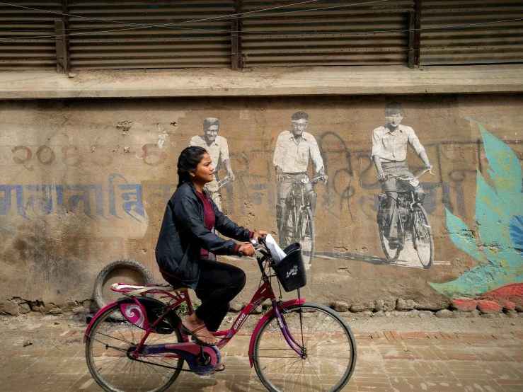 the woman rides her bicycle past a wall with painted murals